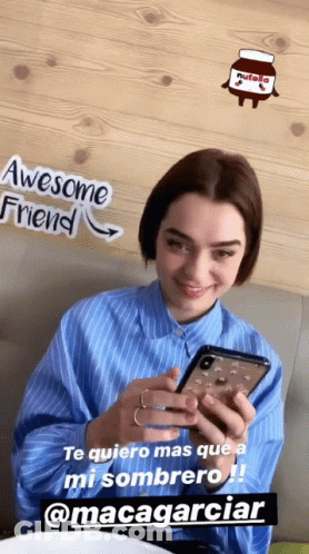 A Woman Is Smiling While Looking At Her Cell Phone With A Nutella Sticker On The Wall Behind Her GIF