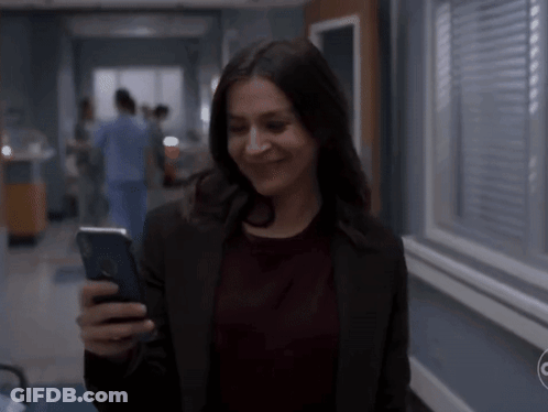 A Woman Is Smiling While Looking At Her Phone GIF