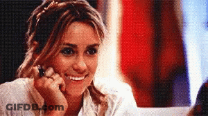 A Woman Is Smiling While Looking At Herself In A Mirror GIF