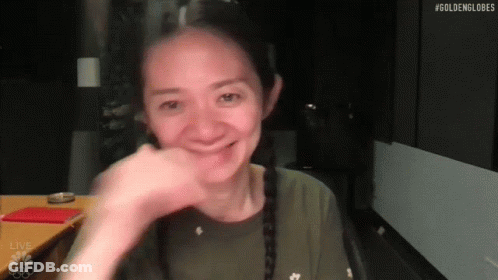 A Woman Is Smiling While Sitting At A Table With Her Hand On Her Face . GIF