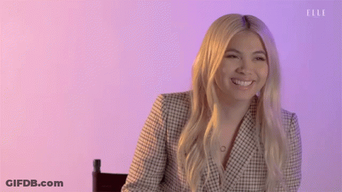 A Woman Is Smiling While Sitting In A Chair In Front Of A Purple Wall . GIF