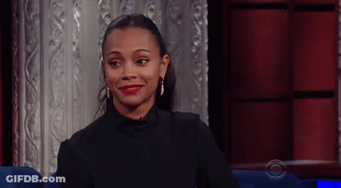 A Woman Is Smiling While Sitting In A Chair In Front Of A Red Curtain . GIF