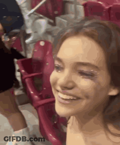 A Woman Is Smiling While Sitting In A Stadium Surrounded By Red Seats GIF