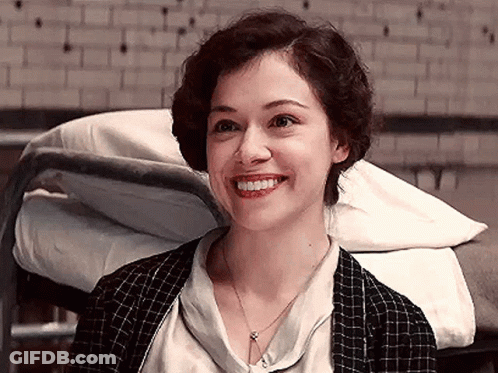 A Woman Is Smiling While Sitting In Front Of A Bed . GIF