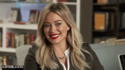A Woman Is Smiling While Sitting In Front Of A Bookshelf . GIF