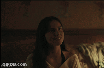 A Woman Is Smiling While Sitting On A Bed In A Dark Room GIF