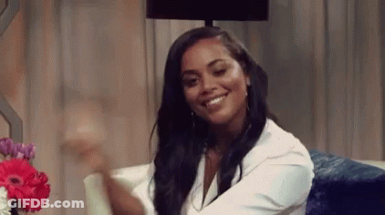 A Woman Is Smiling While Sitting On A Couch Next To A Lamp . GIF