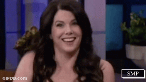 A Woman Is Smiling While Sitting On A Stage In Front Of A Purple Wall . GIF
