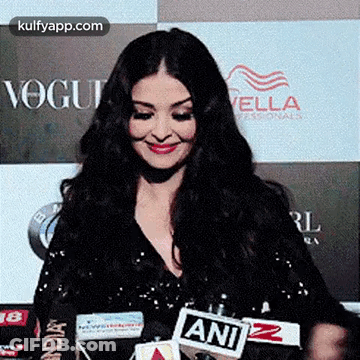A Woman Is Smiling While Standing In Front Of A Microphone . GIF
