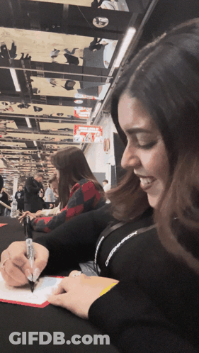 A Woman Is Smiling While Writing On A Piece Of Paper With A Pen GIF