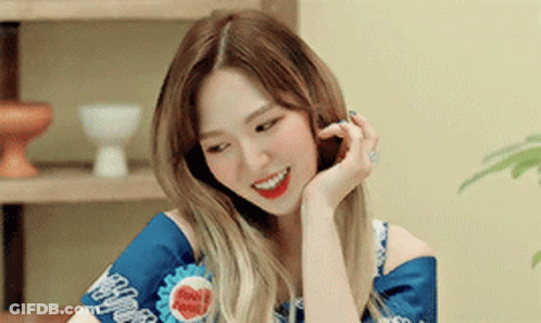 A Woman Is Smiling With Her Hand On Her Face While Wearing A Blue Shirt . GIF