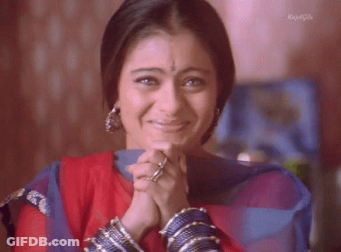 A Woman Is Smiling With Her Hands Folded In Front Of Her Face And The Words Kajal Girls On The Bottom GIF