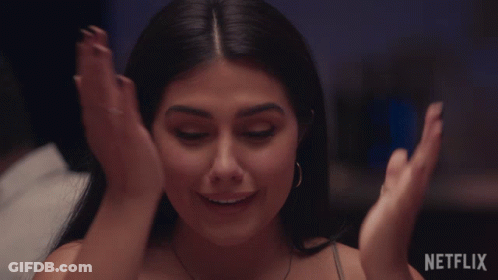 A Woman Is Smiling With Her Hands On Her Face In Front Of A Netflix Sign GIF