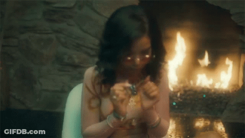 A Woman Is Smoking A Cigarette In Front Of A Fire GIF