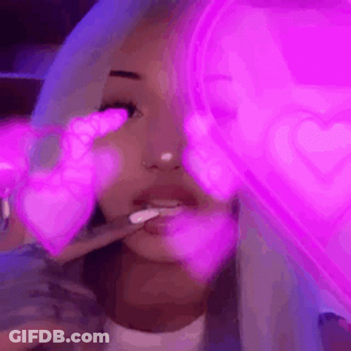A Woman Is Smoking A Cigarette In Front Of A Neon Heart . GIF