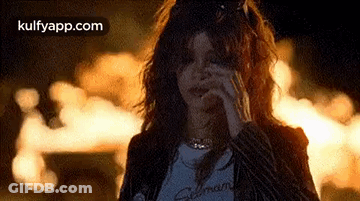 A Woman Is Smoking A Cigarette While Standing In Front Of A Fire At Night . GIF