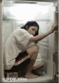 A Woman Is Squatting In An Open Refrigerator Looking For Something To Eat . GIF
