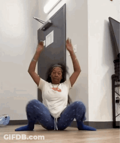 A Woman Is Squatting On The Floor In Front Of A Door With Her Hands In The Air . GIF
