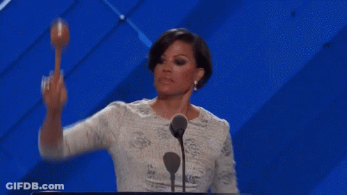 A Woman Is Standing At A Podium With A Microphone And Holding A Maracas In Her Hand . GIF