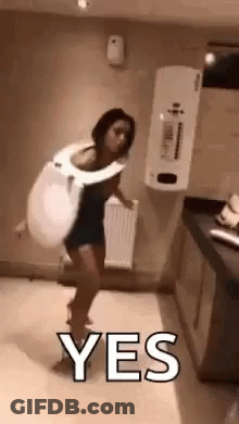 A Woman Is Standing In A Bathroom Wearing A Toilet Seat And Holding A Toilet Seat . GIF