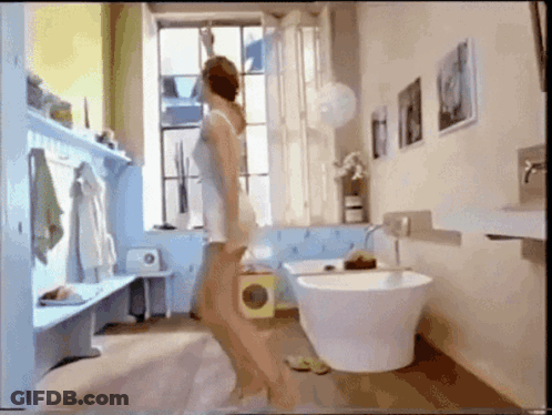 A Woman Is Standing In A Bathroom With A Bathtub GIF