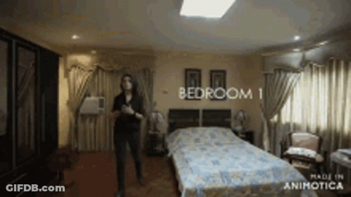 A Woman Is Standing In A Bedroom That Says Bedroom 1 GIF