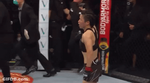 A Woman Is Standing In A Boxing Ring With A Body Armor Drink In The Background . GIF