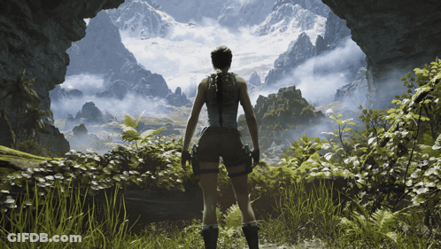 A Woman Is Standing In A Cave Looking Out At A Mountain Range GIF