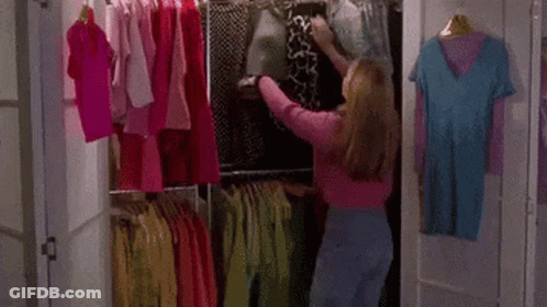 A Woman Is Standing In A Closet Filled With Clothes And Picking A Shirt . GIF