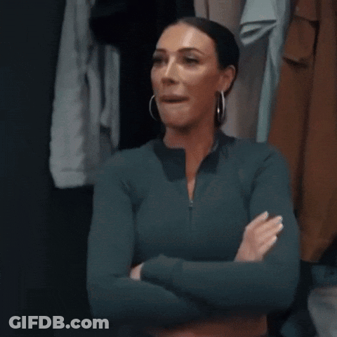 A Woman Is Standing In A Closet With Her Arms Crossed And Looking At The Camera . GIF