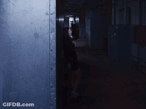 A Woman Is Standing In A Dark Hallway With A Light On GIF