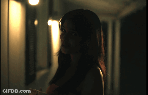 A Woman Is Standing In A Dark Hallway With A Light Shining On Her GIF