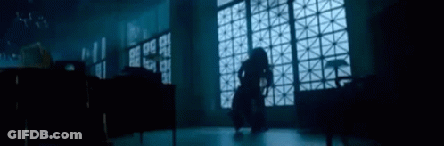 A Woman Is Standing In A Dark Room In Front Of A Large Window . GIF