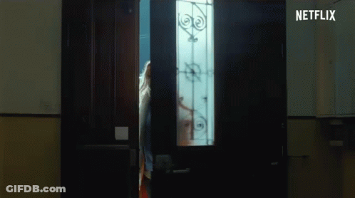 A Woman Is Standing In A Dark Room Looking Out Of A Doorway . GIF