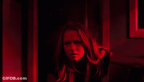 A Woman Is Standing In A Dark Room With A Red Light Behind Her . GIF