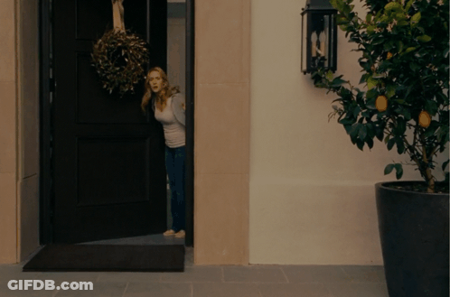 A Woman Is Standing In A Doorway With A Wreath Hanging From It GIF