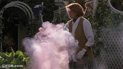 A Woman Is Standing In A Garden With Smoke Coming Out Of Her Hand GIF
