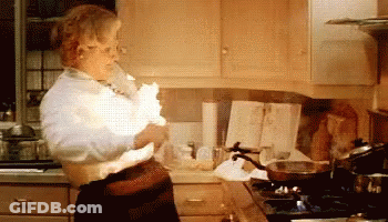 A Woman Is Standing In A Kitchen Holding A Piece Of Paper That Is Exploding . GIF