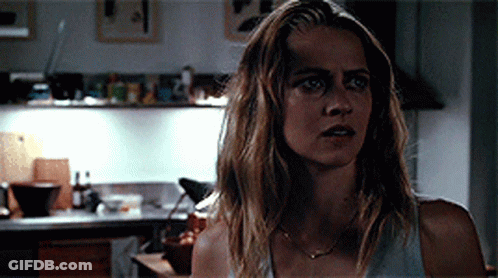 A Woman Is Standing In A Kitchen Wearing A White Tank Top GIF