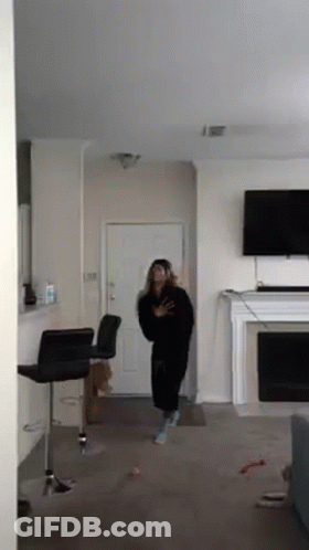 A Woman Is Standing In A Living Room In Front Of A Fireplace And Television . GIF