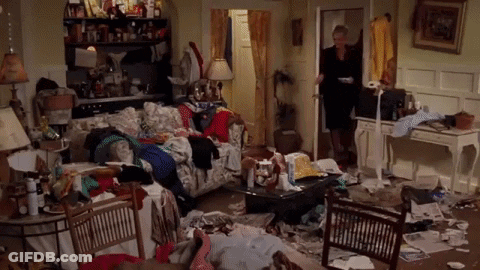 A Woman Is Standing In A Messy Living Room Filled With Lots Of Clothes And Papers . GIF