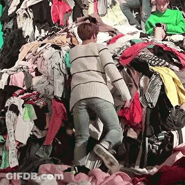 A Woman Is Standing In A Pile Of Clothing GIF