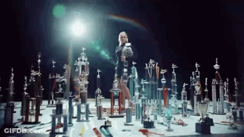 A Woman Is Standing In A Room Filled With Trophies And Awards . GIF