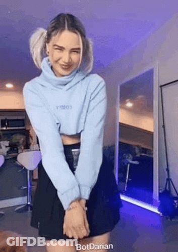 A Woman Is Standing In A Room Wearing A Blue Sweater And A Black Skirt . GIF