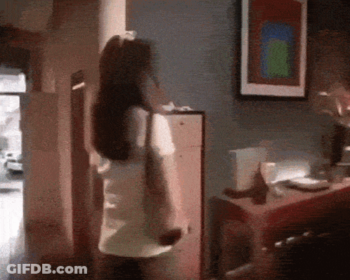 A Woman Is Standing In A Room With A Picture On The Wall Above Her GIF