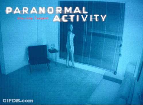 A Woman Is Standing In A Room With The Words Paranormal Activity GIF