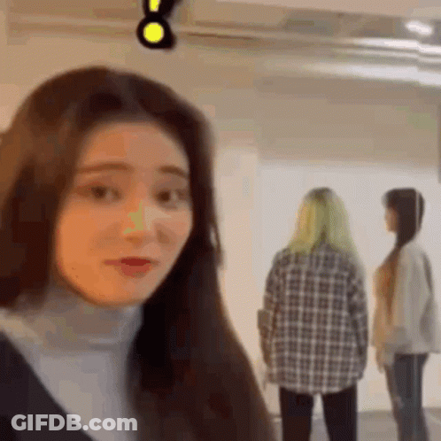 A Woman Is Standing In A Room With Two Other Women And Looking At The Camera . GIF