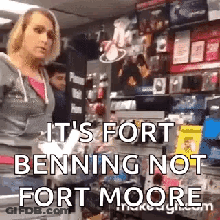 A Woman Is Standing In A Store With The Words `` It 'S Fort Benning Not Fort Moore '' Written On Her Face . GIF