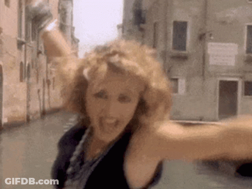A Woman Is Standing In A Street With Her Arms Outstretched And A Building In The Background . GIF