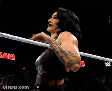 A Woman Is Standing In A Wrestling Ring Holding A Rope And Looking At The Camera . GIF